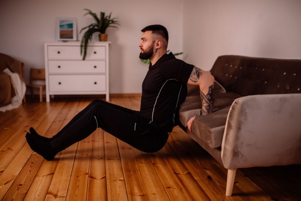 pexels-photo-10815903-10815903 A bearded man in black fitness attire exercising at home, showcasing arm tattoos and a healthy lifestyle.