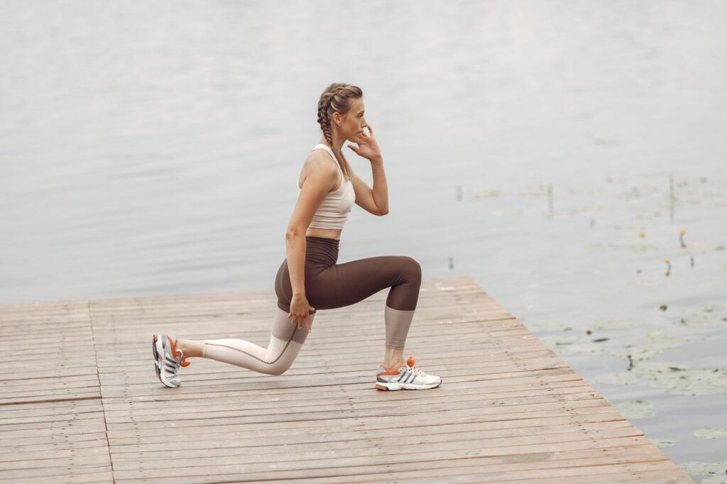 pexels-photo-4971063-4971063 A woman performs lunges on a lakeside wooden deck, showcasing a fit lifestyle outdoors.
